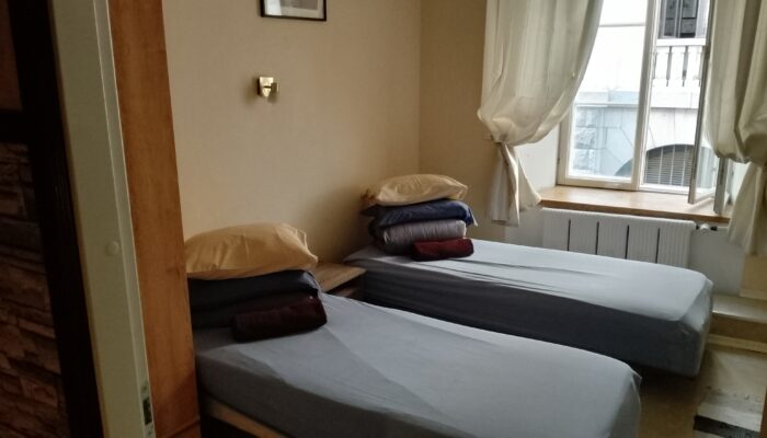Room with 2 parallel beds, with new linen and towel. There is a large window on the wall, with curtains