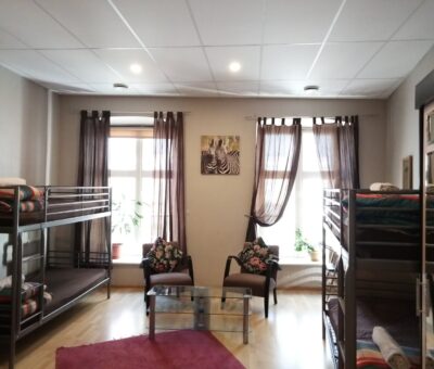 Big room with classic furniture. There are bunk beds on the left and right, and armchairs in the middle. The background wall has two large windows with curtains